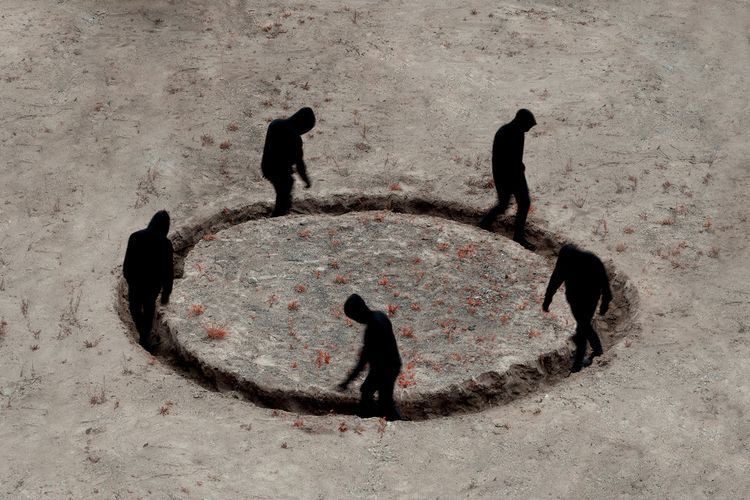 Hooded figures walking around a circular pit